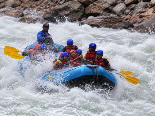 Rafters paddling and hitting strong Roller Coaster rapids during rafting in Rishikesh