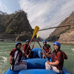 Friends enjoying river rafting with paddles and scenic mountain bridges in Rishikesh